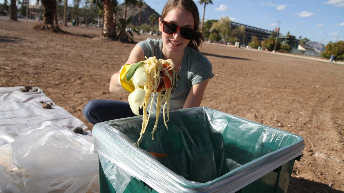 A girl wearing a rubber glove holds a handful of food waste. 