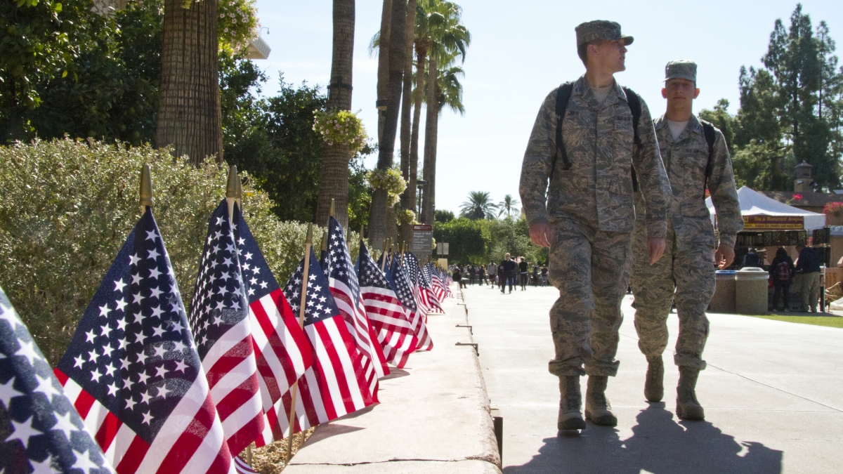 men in military uniforms walking along line of flags on campus