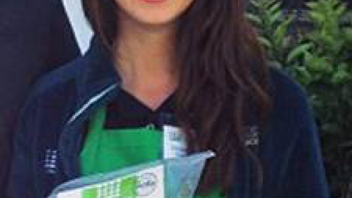 Natalie Fleming with brown hair wearing green apron holding compost bag