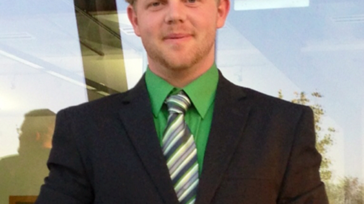 blonde haired Bradley Baker wearing black suit and green shirt and tie standing