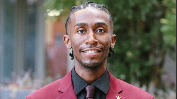 A man in a maroon suit smiles for the camera.