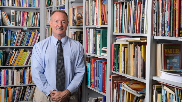 ASU English Professor James Blasingame standing in his office surrounded by shelves of books