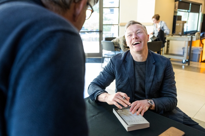 Man laughing and chatting with someone while signing book